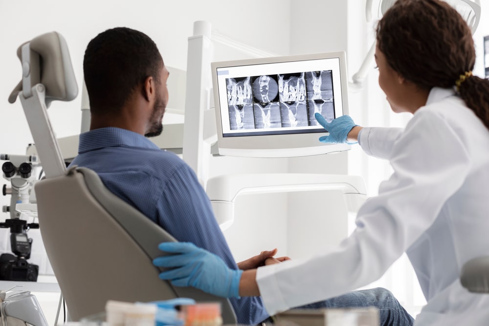 African,Female,Dentist,And,Male,Patient,Watching,Xray,On,Digital