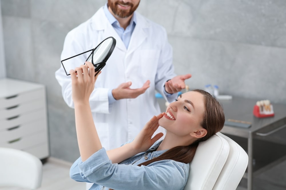 Young,Woman,Looking,At,Her,New,Dental,Implants,In,Mirror